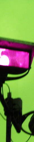 A blurry, evening shot of a light on top of a building. The dark, blue sky has been shifted to green and the bright, yellow light has been shifted to magenta, courtesy of photoshop.