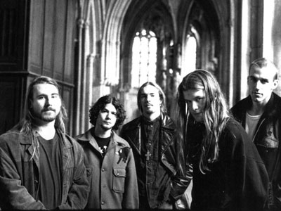 A picture of the members of Blind Melon wearing coats and standing together in a cathedral.
