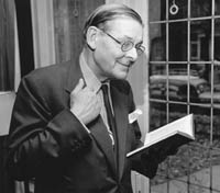 Photo of T. S. Eliot smiling and reading from a book with his other hand grasping the fold of his suit.