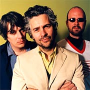 An image of band members from The Flaming Lips standing in front of a yellow background doing nothing in particular.