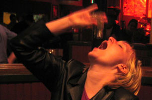 A photograph of Mindy sitting in a bar, visibly drunk, downing a pepper shaker.