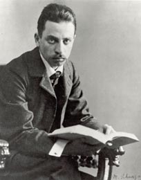 Image of Rainier Maria Rilke looking ahead while seated in an old chair with a book in his hands.
