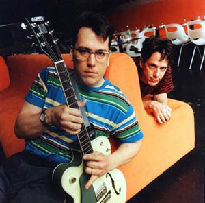 Photo of the Johns from They Might Be Giants on a big orange chair with Flansburgh in front and Linnell in back (This is a link to their website).