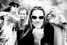 A photograph of the Ugly Kid Joe band members standing together with the sky and clouds behind them.